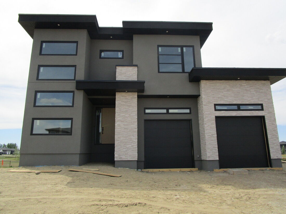 The same house finished in dark grey stucco with stone feature walls and black garage doors