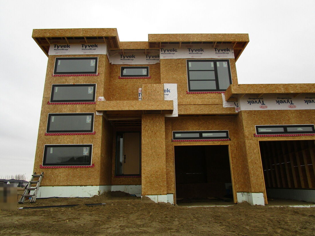 Front of a new modern house wrapped in sheathing, with garage openings