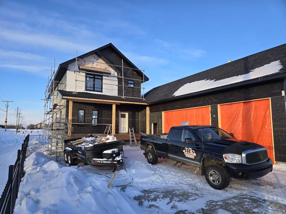 New two-storey house with a covered porch, black base coat and scaffolding, and a garage covered in orange tarp
