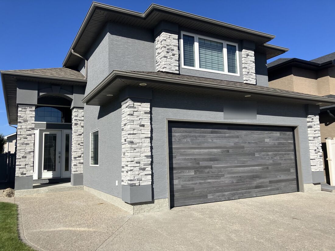 The same house finished in dark grey stucco with white stacked stone columns and a wood-look garage door