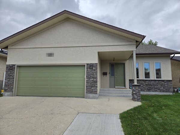 Stucco bungalow with a green garage door and stone columns