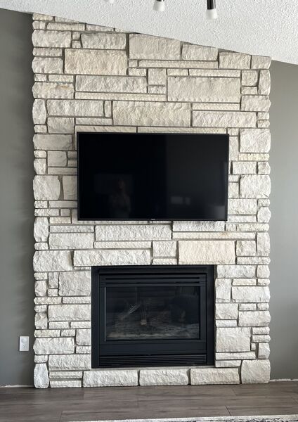 White stone fireplace wall with a television above