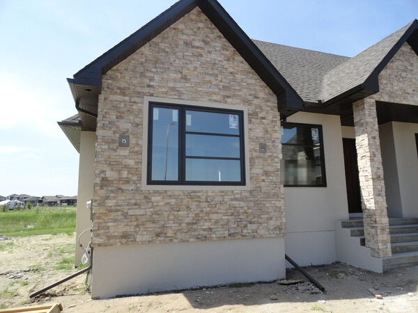 Stone and stucco house front with a gable of stacked stone, black eavestrough and dark soffit