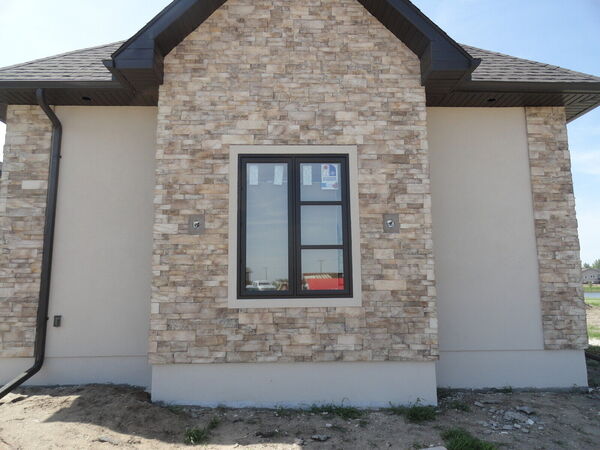 Stacked-stone panel around a window on a stucco wall with a black downspout