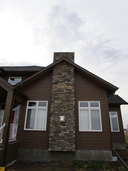 Side of a brown siding house with a stone chimney