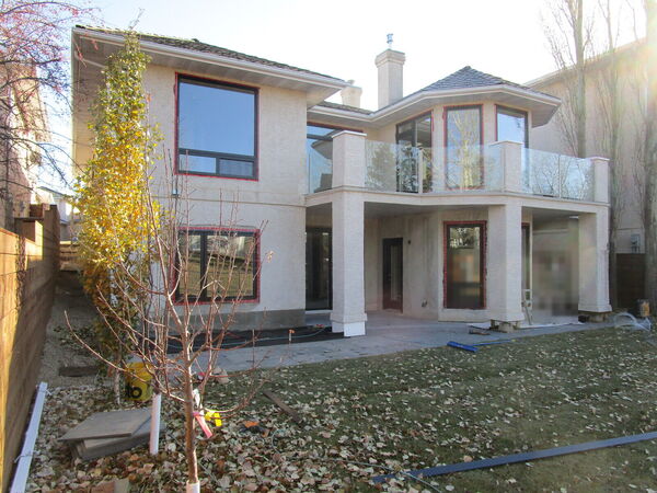 Back of a two-storey stucco house with a glass balcony railing and stucco columns