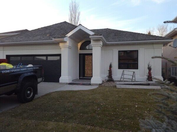 White stucco bungalow with columns at the entry and a dark garage door