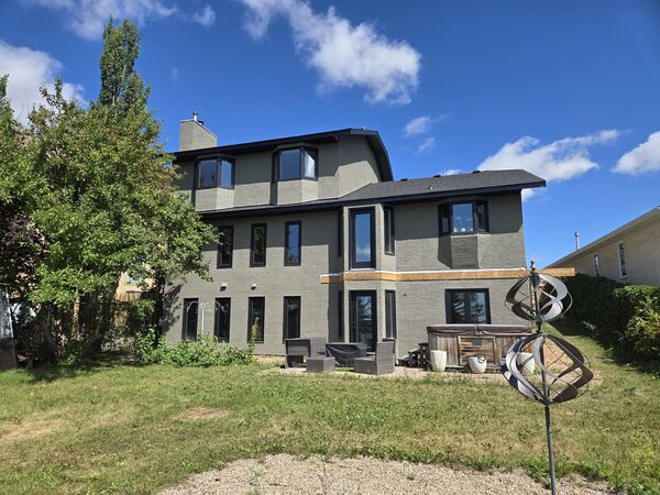Back of a three-storey house in grey stucco with dark windows and a cedar-coloured band