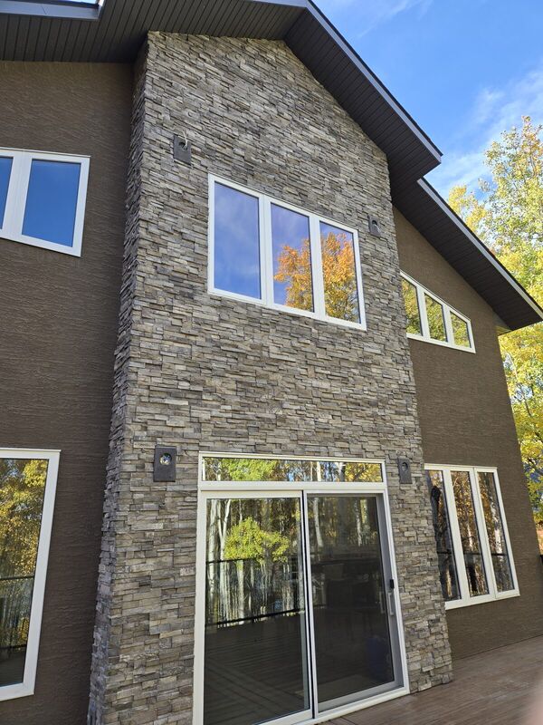 Stacked stone feature wall with large windows and sliding doors on a brown stucco house