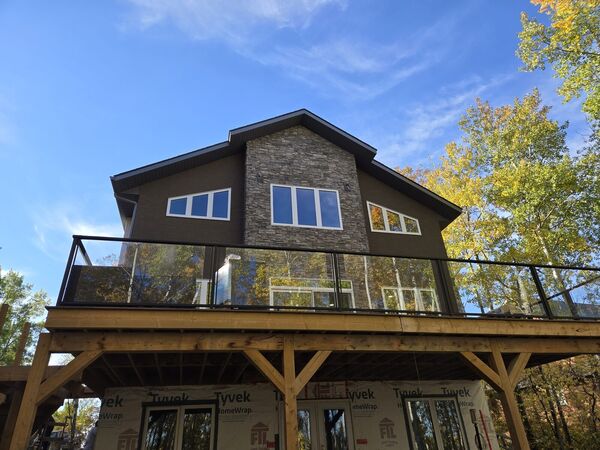 Back of a two-storey house with brown stucco, a stone feature wall and a glass-railed deck