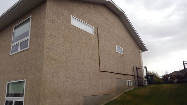 Side of a house with weathered brown stucco and a long cable run