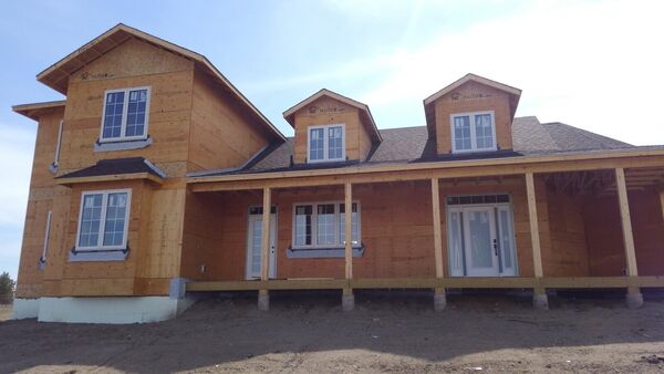 Farmhouse-style house wrapped in sheathing with dormers and a covered porch